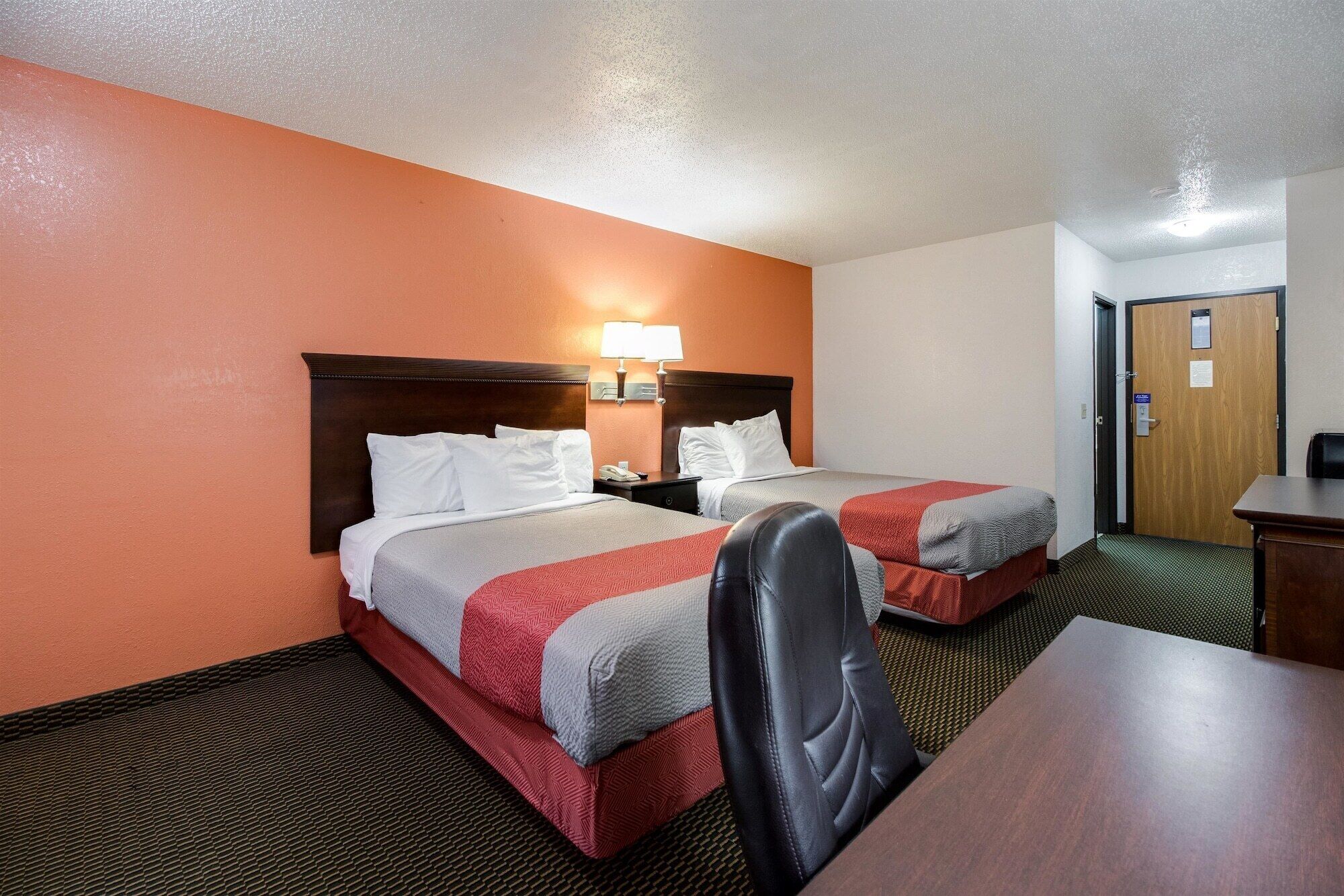 A hotel room with two beds, a desk, and a chair.