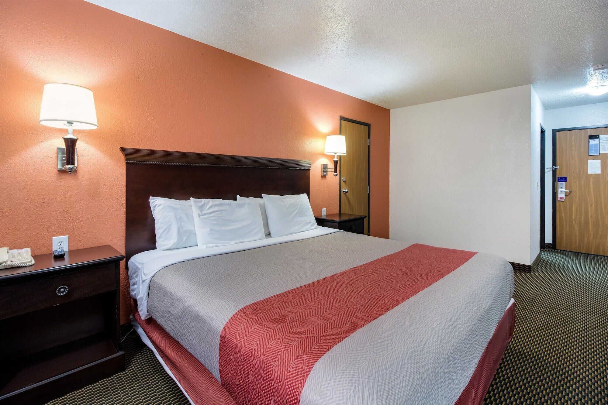 A hotel room with a large bed, two bedside tables with lamps, a wooden headboard, and a door with a sign.
