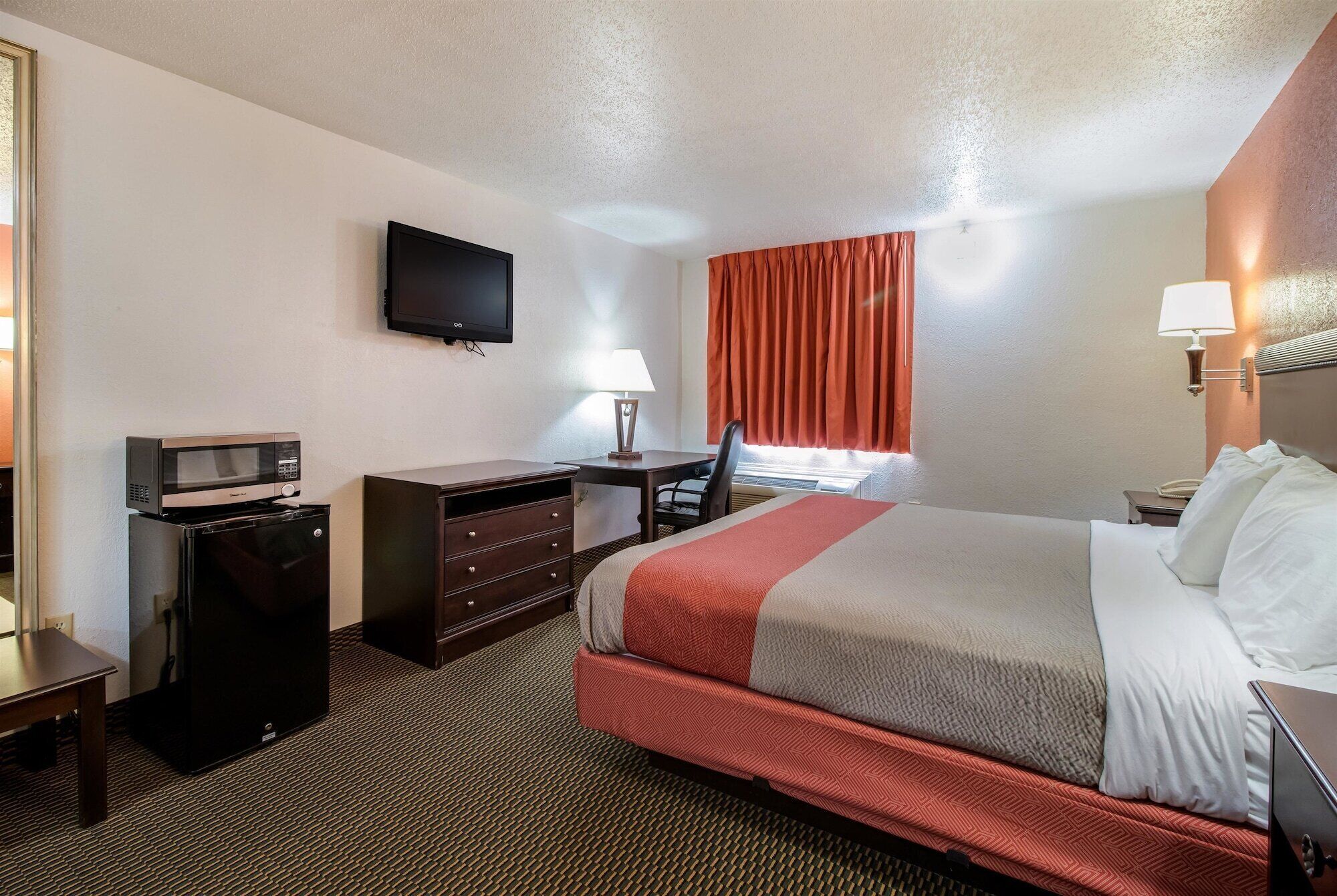 Habitación de hotel con cama, escritorio, computadora, televisor y microondas.