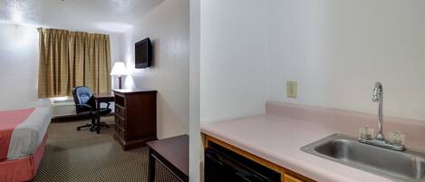 Habitación de hotel con cama, escritorio, silla, lámpara, televisión y kitchenette con pileta.