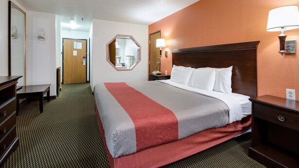 A hotel room with a bed, a desk, a dresser, a mirror, and a nightstand with a lamp. - Motel 6 Marion, IL (Marion)
