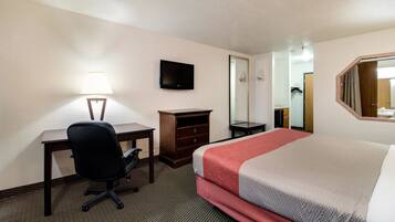 Habitación de hotel con cama, escritorio con silla, cómoda, televisor de pantalla plana, espejo y lámpara.