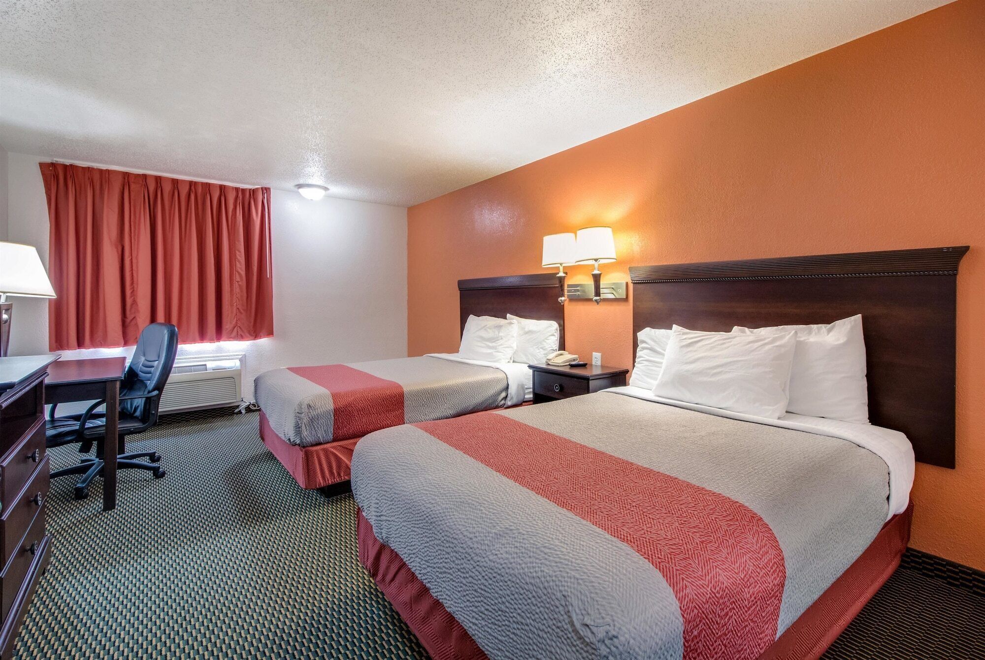 A hotel room with two beds, a desk, and a chair.