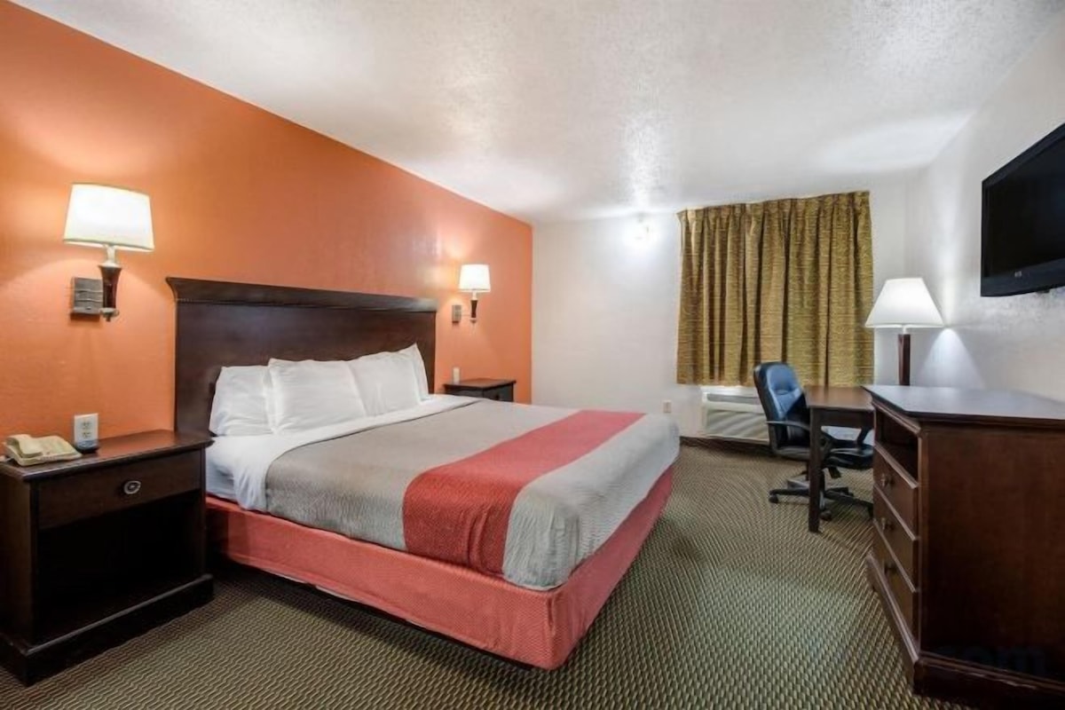 A hotel room with a bed, bedside tables, a desk, a chair, and a television.