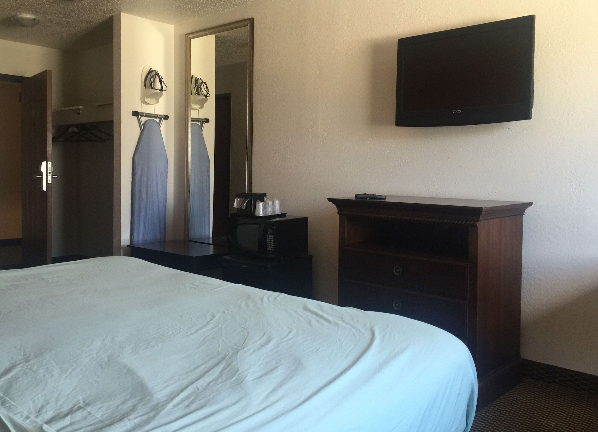A hotel room with a large bed, a flat-screen TV mounted on the wall, a wooden dresser, and a mirror.