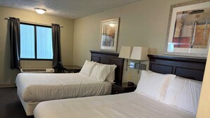 A hotel room with two beds, a desk, a chair, a window with curtains, an air conditioning unit, and a framed picture on the wall. - Boarders Inn & Suites by Cobblestone Hotels – Broken Bow (Broken Bow)