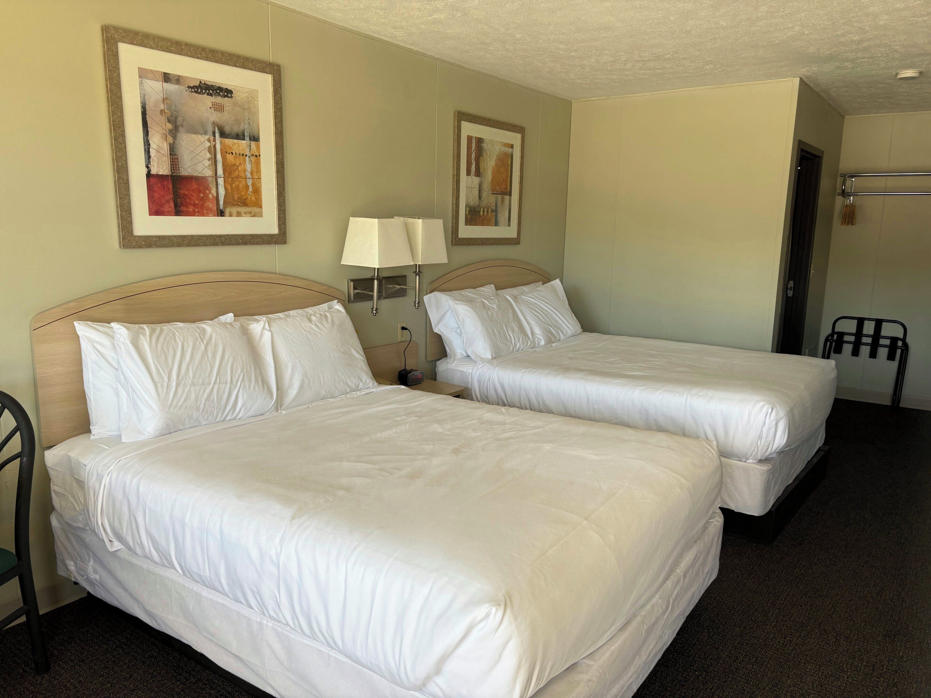 A hotel room with two beds, a nightstand with a lamp, and artwork on the walls.