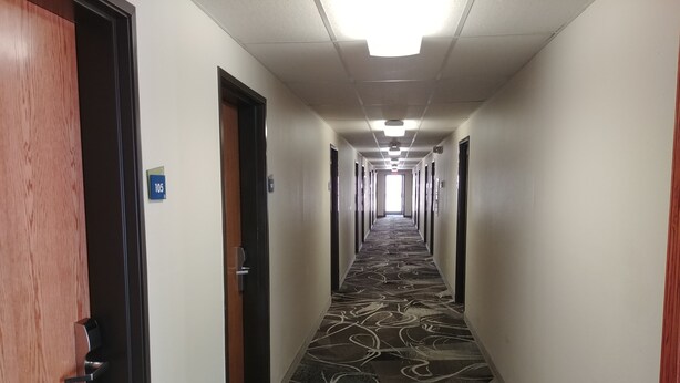 A hotel hallway with carpeted floors, doors on both sides, and a sign indicating room number 105. - Boarders Inn & Suites by Cobblestone Hotels – Broken Bow (Broken Bow)