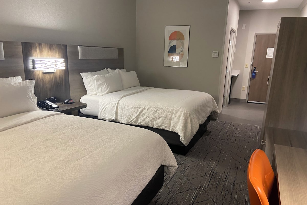 A hotel room with two beds, a nightstand, a telephone, a wall-mounted light, and a door.