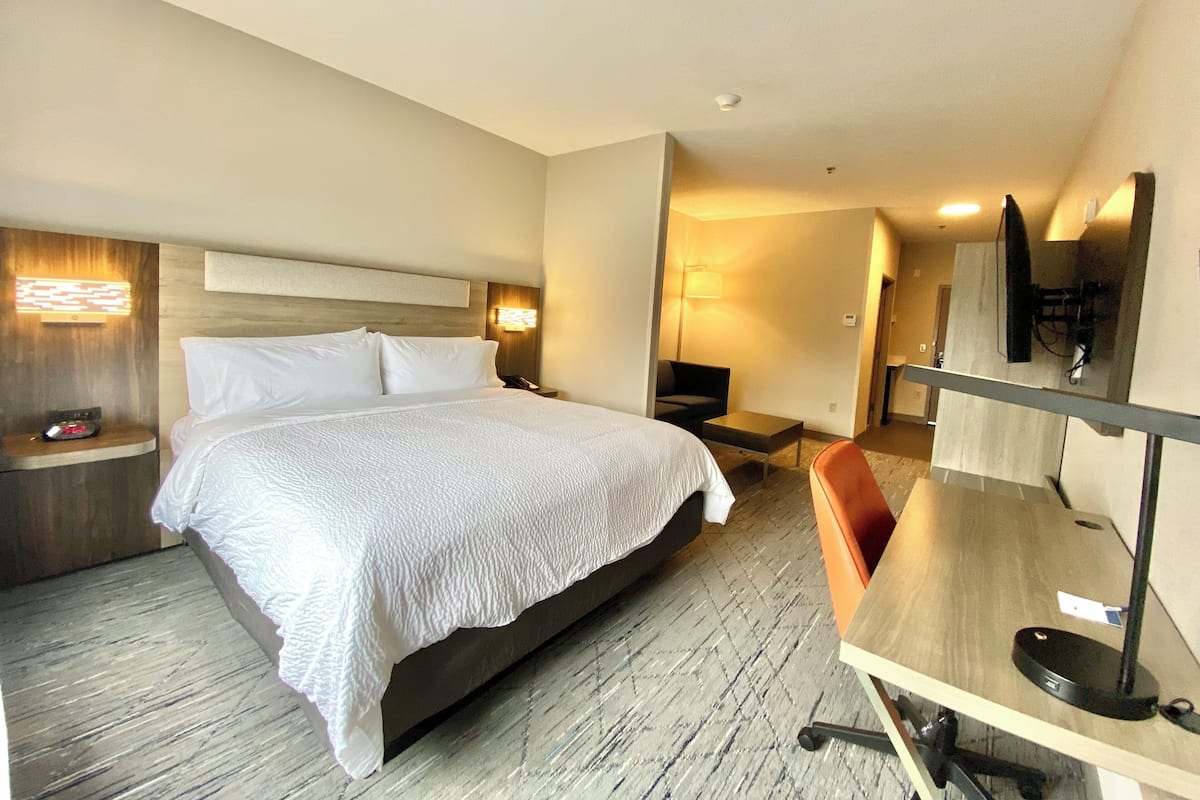 A hotel room with a large bed, bedside tables, a desk with a chair, a flat-screen TV, and a lamp.