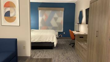 Une chambre d’hôtel comprenant un lit, un bureau, une chaise, une armoire et un mur agrémenté d’un store à motifs géométriques.