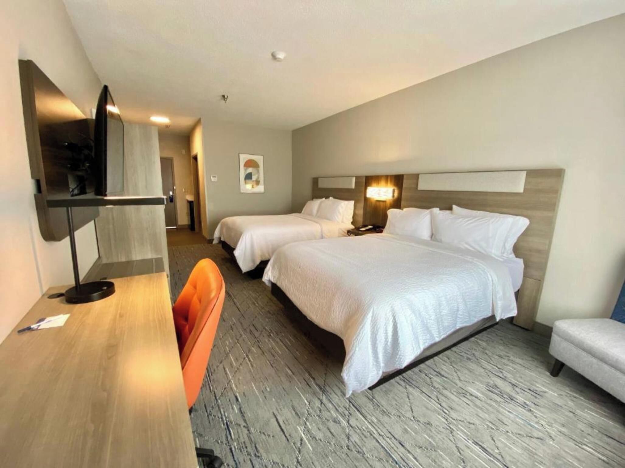 Ein Hotelzimmer mit zwei Betten, einem Schreibtisch, einem Stuhl, einem Fernseher und einem kleinen Tisch.