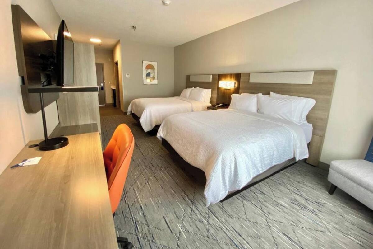 A hotel room with two beds, a desk, a chair, a TV, and a small table.