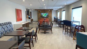 A modern dining area with multiple tables and chairs, a flat-screen TV mounted on the wall, and a coffee station. - Holiday Inn Express & Suites Elyria by IHG (Elyria)