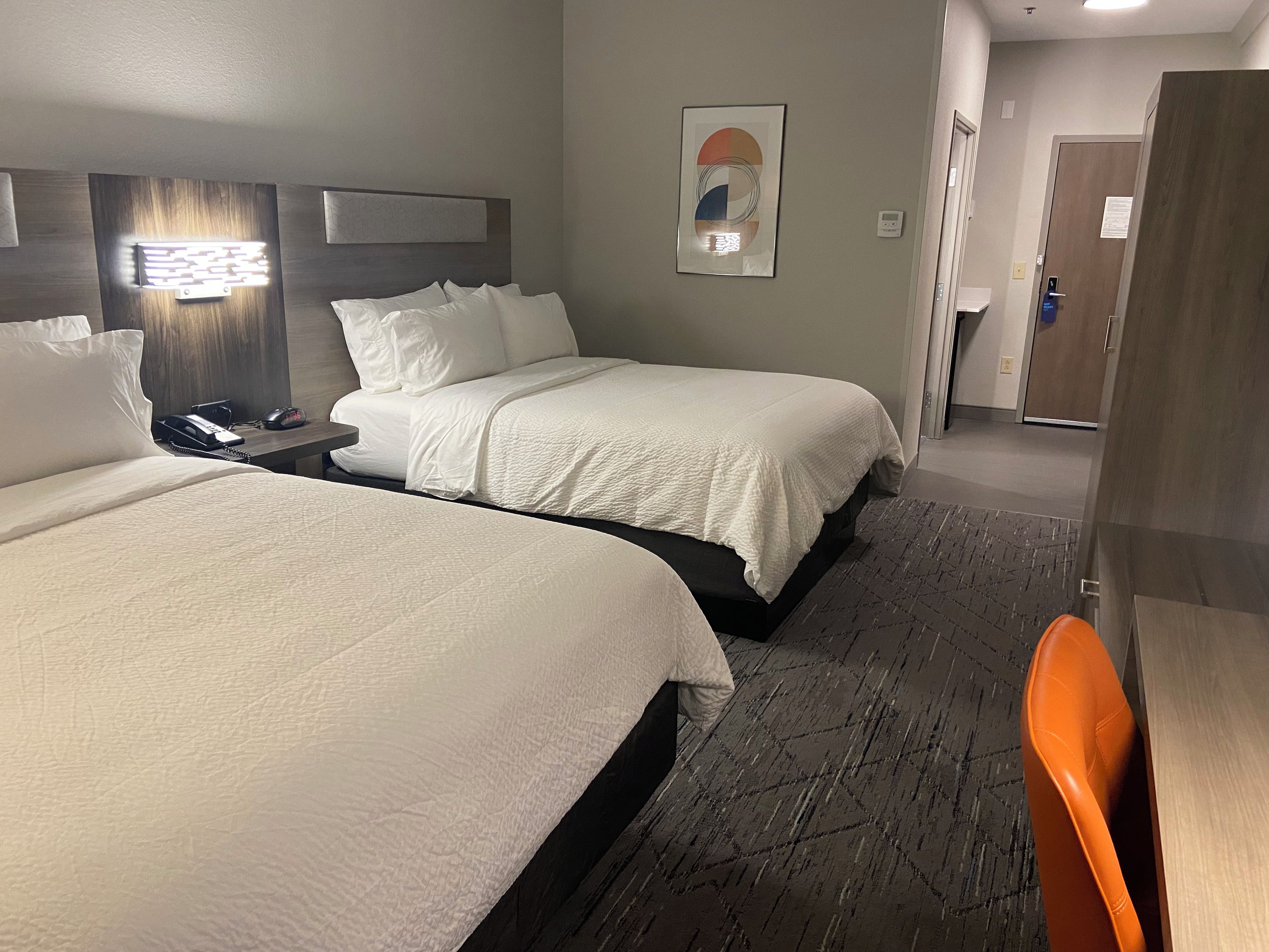 A hotel room with two beds, a nightstand, a telephone, a wall-mounted light, and a door.
