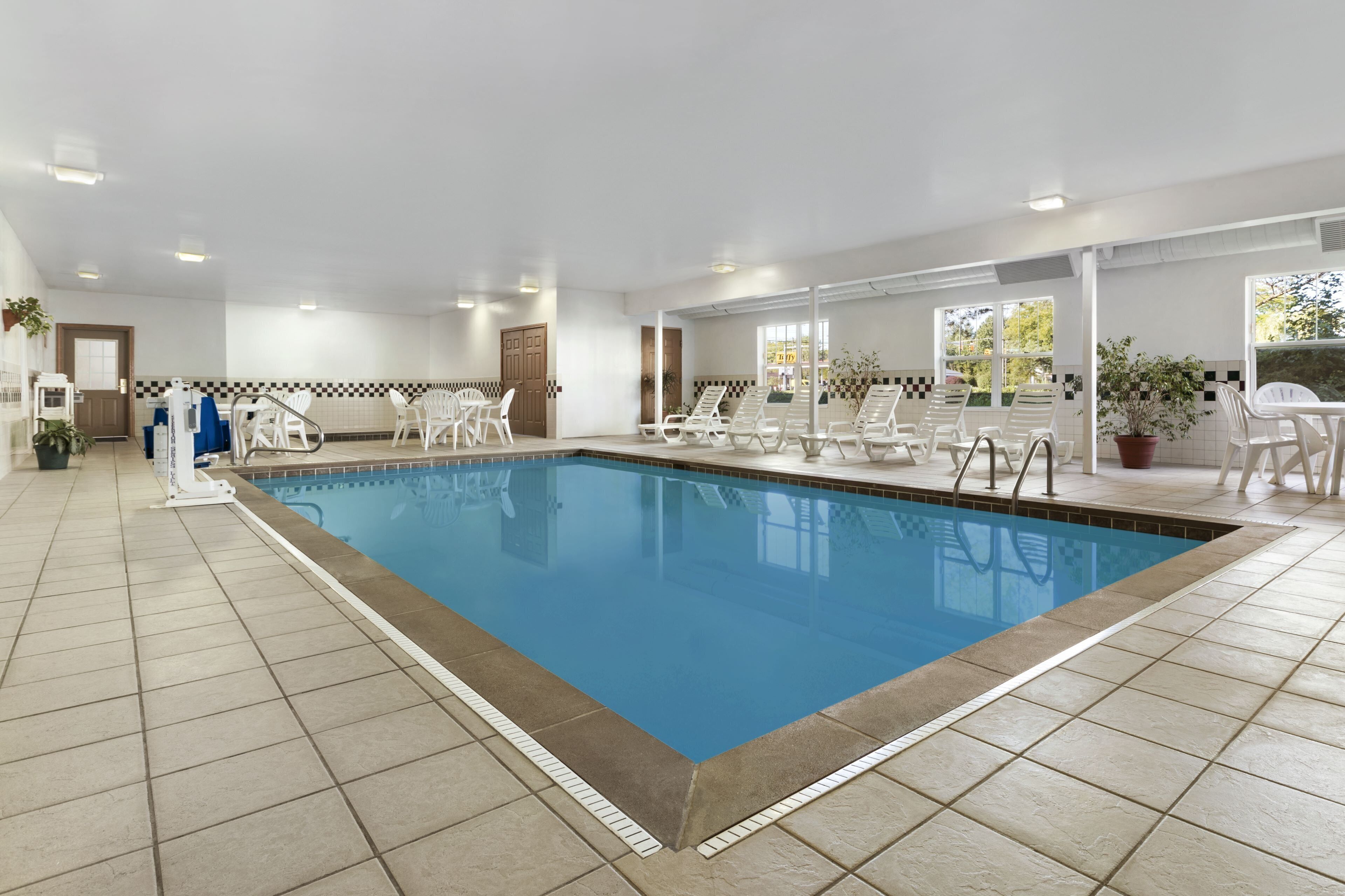 A swimming pool with tiled flooring, white lounge chairs, and a door leading to a changing room.