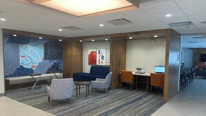 A modern waiting area with a blue sofa, two armchairs, a small table, and a computer desk with a printer. - Holiday Inn Express & Suites Elyria by IHG (Elyria)