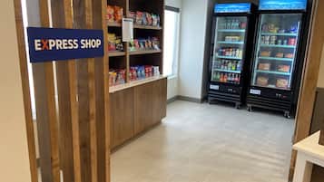 A retail area with a sign for an Express Shop, shelves stocked with snacks, and two refrigerated beverage dispensers.