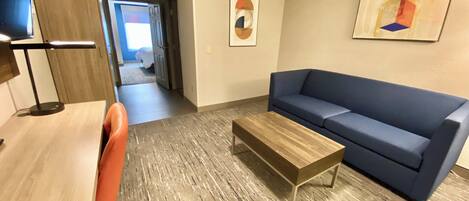 A modern living room with a sofa, a coffee table, and a desk with a chair. There is a hallway leading to another room.