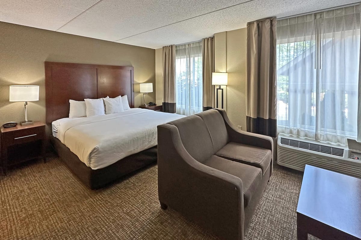 A hotel room with a large bed, a chair, a desk, and two lamps.