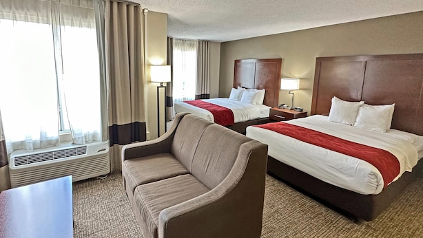 A hotel room with two beds, a sofa, a desk, and a window with curtains. - Concord Suites (Concord)