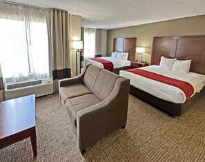Ein Hotelzimmer mit zwei Betten, einem Schlafsofa, einem Schreibtisch und einem Fenster mit Vorhängen.
