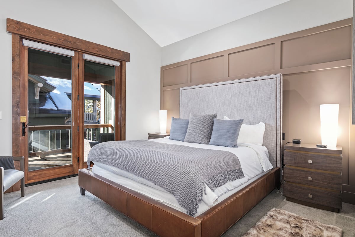 A bedroom with a large bed, wooden headboard, and a sliding glass door leading to a balcony.