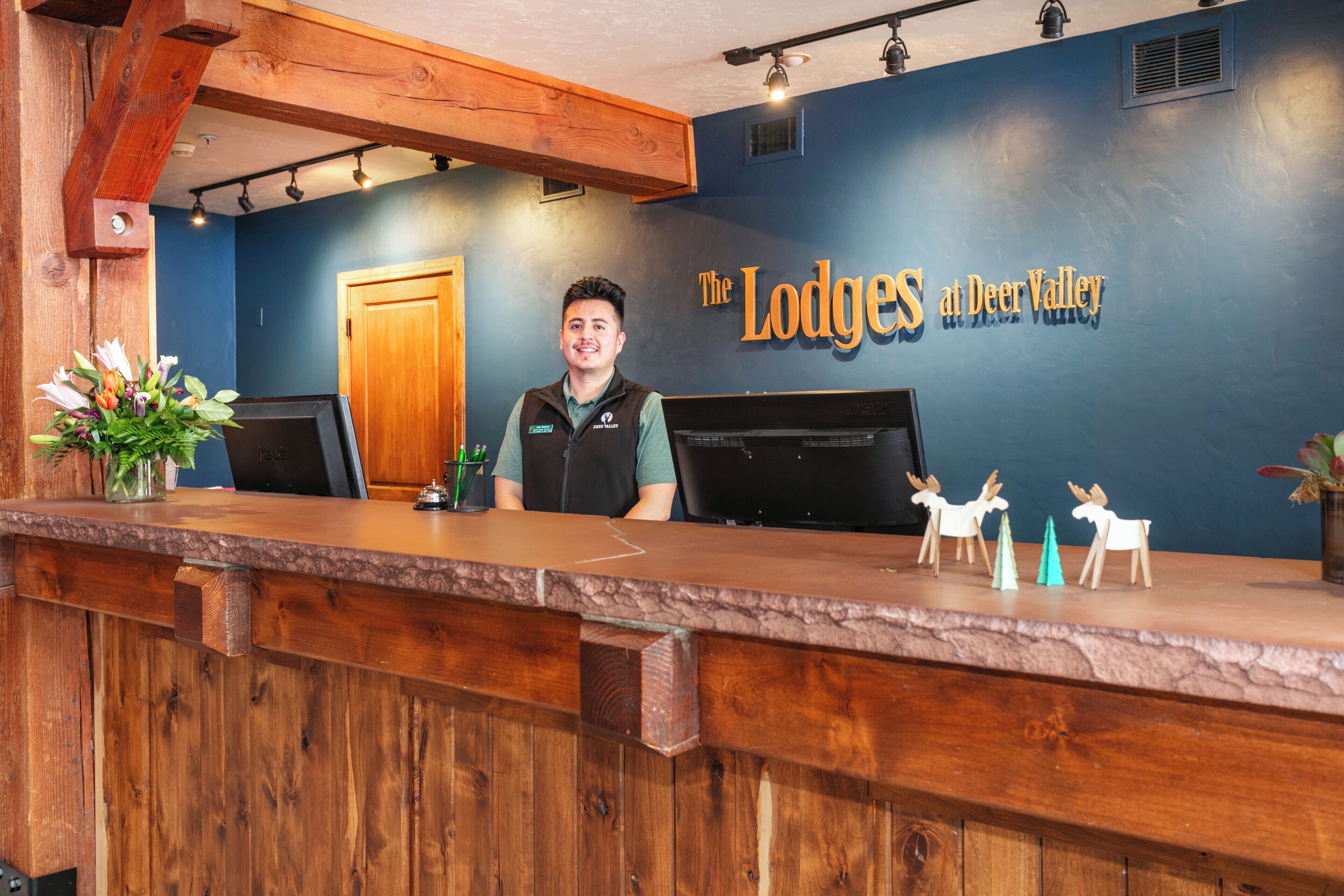 A reception desk at The Lodges at Deer Valley with a wooden counter, a welcome sign, and a small plant.