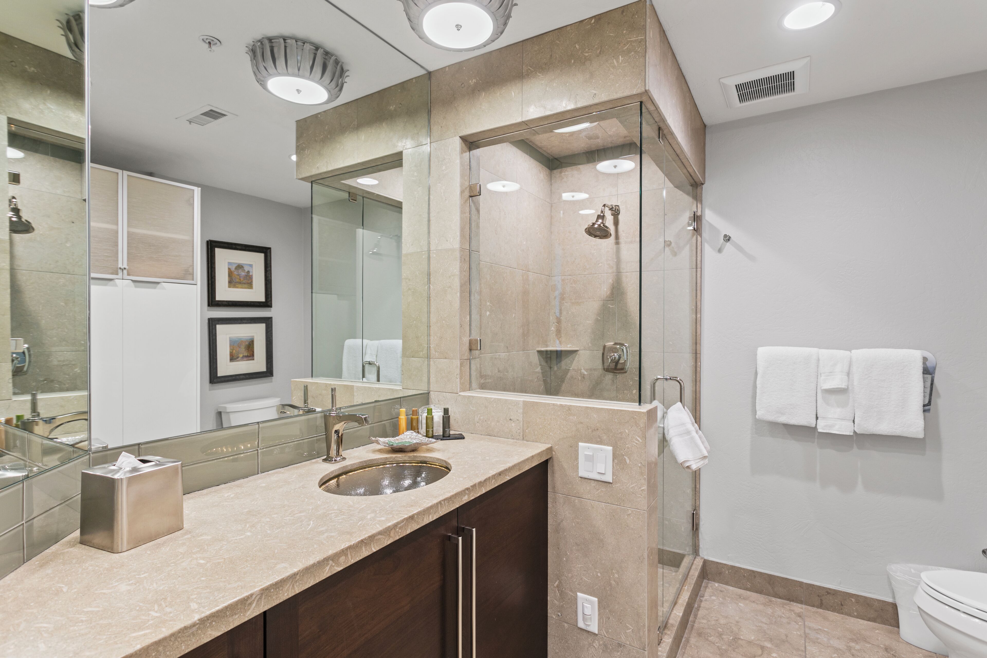 A modern bathroom with a large mirror, a sink, and a glass-enclosed shower.