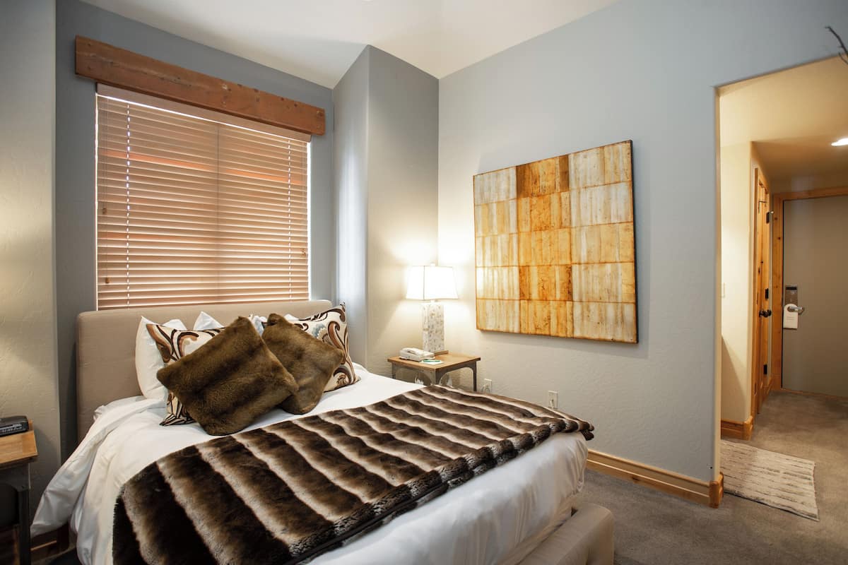 A bedroom with a bed, a nightstand, a lamp, and a painting on the wall.