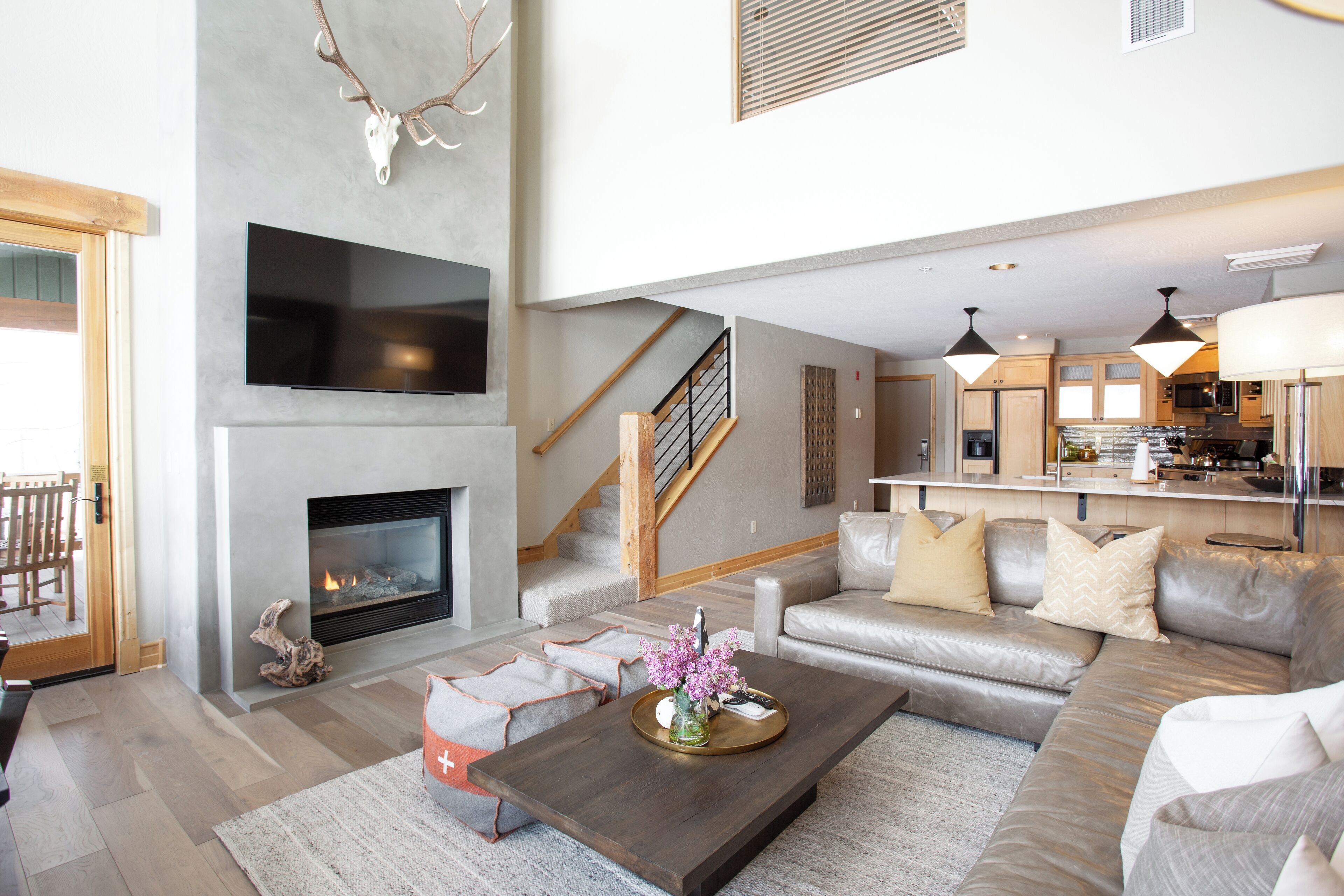 A modern living room with a fireplace, a large flat-screen TV, a sofa set, and a kitchen area in the background.