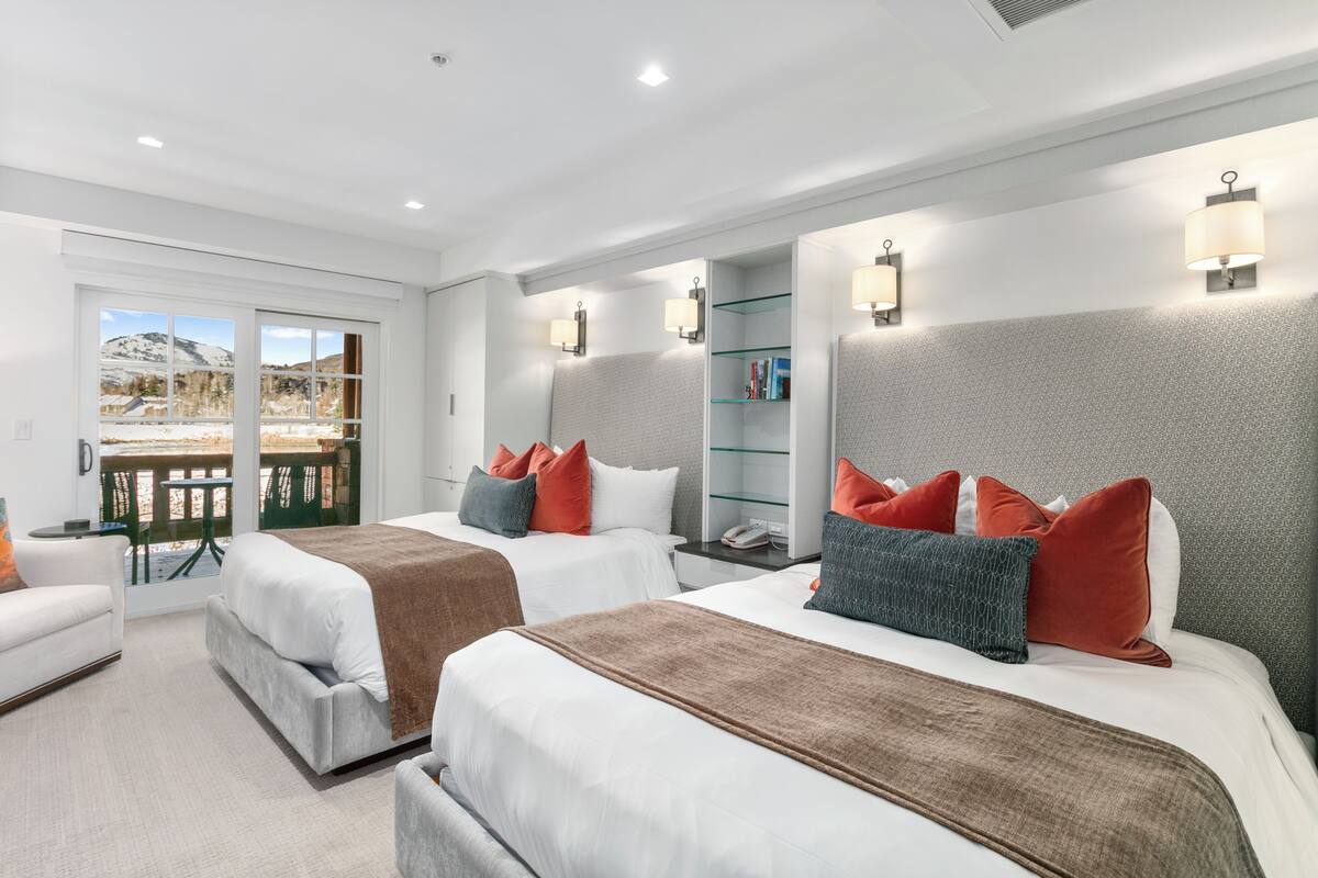 A hotel room with two beds, a sofa, a glass table, and a view of a snowy landscape.