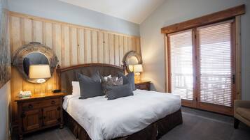 A bedroom with a large bed, wooden headboard, two bedside lamps, and a large window with blinds.