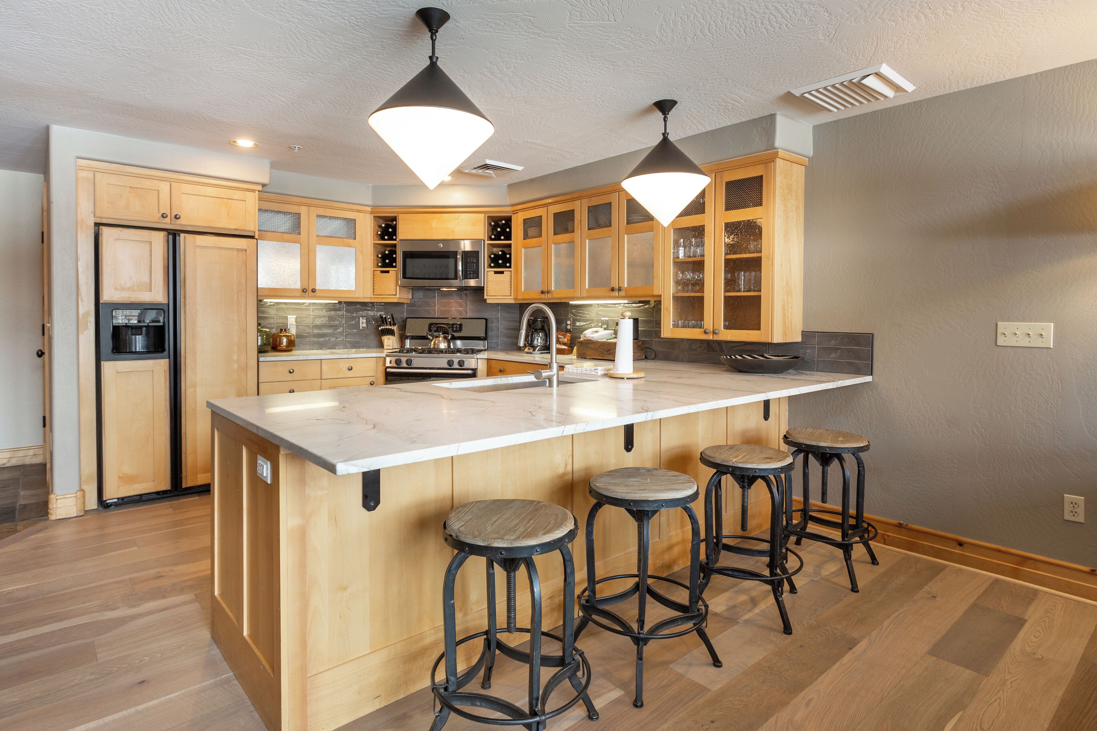 Une cuisine moderne avec des meubles en bois, un grand îlot central doté de tabourets, des appareils en acier inoxydable et un éclairage suspendu.