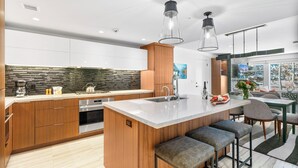 Cozinha moderna com armários de madeira, uma ilha grande com banquetas, eletrodomésticos de aço inoxidável e iluminação pendente.