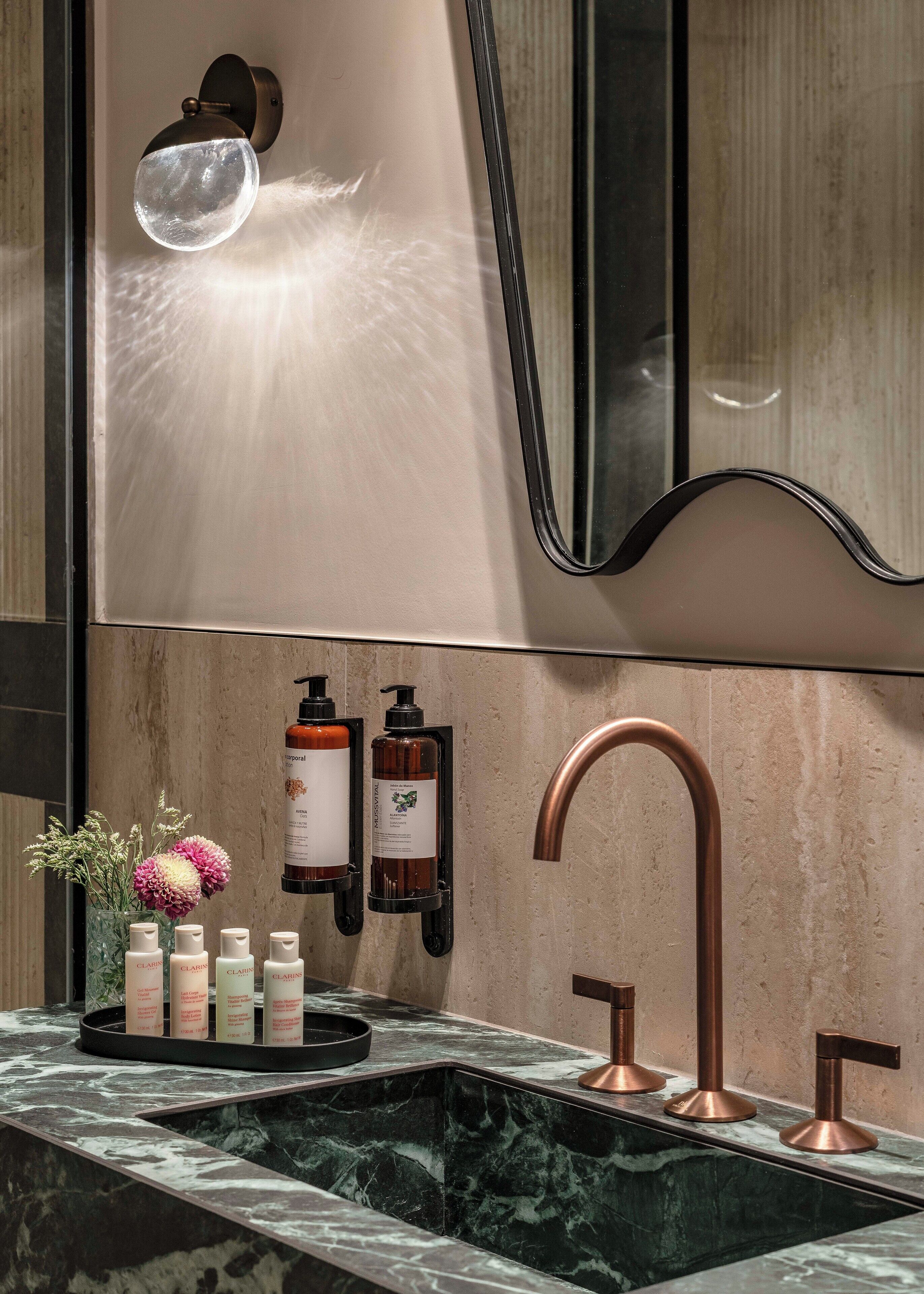 A bathroom with a marble sink, copper faucet, and a wall-mounted mirror.