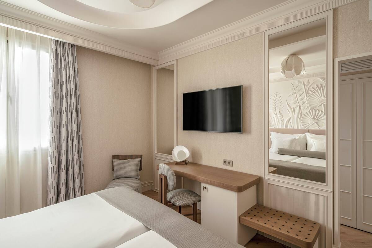 A hotel room with a bed, a desk with a chair, a television, and a mirror.