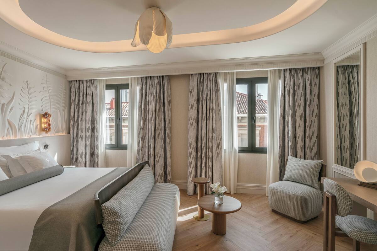 A modern hotel room with a large bed, a sofa, a small table with flowers, and a chair.