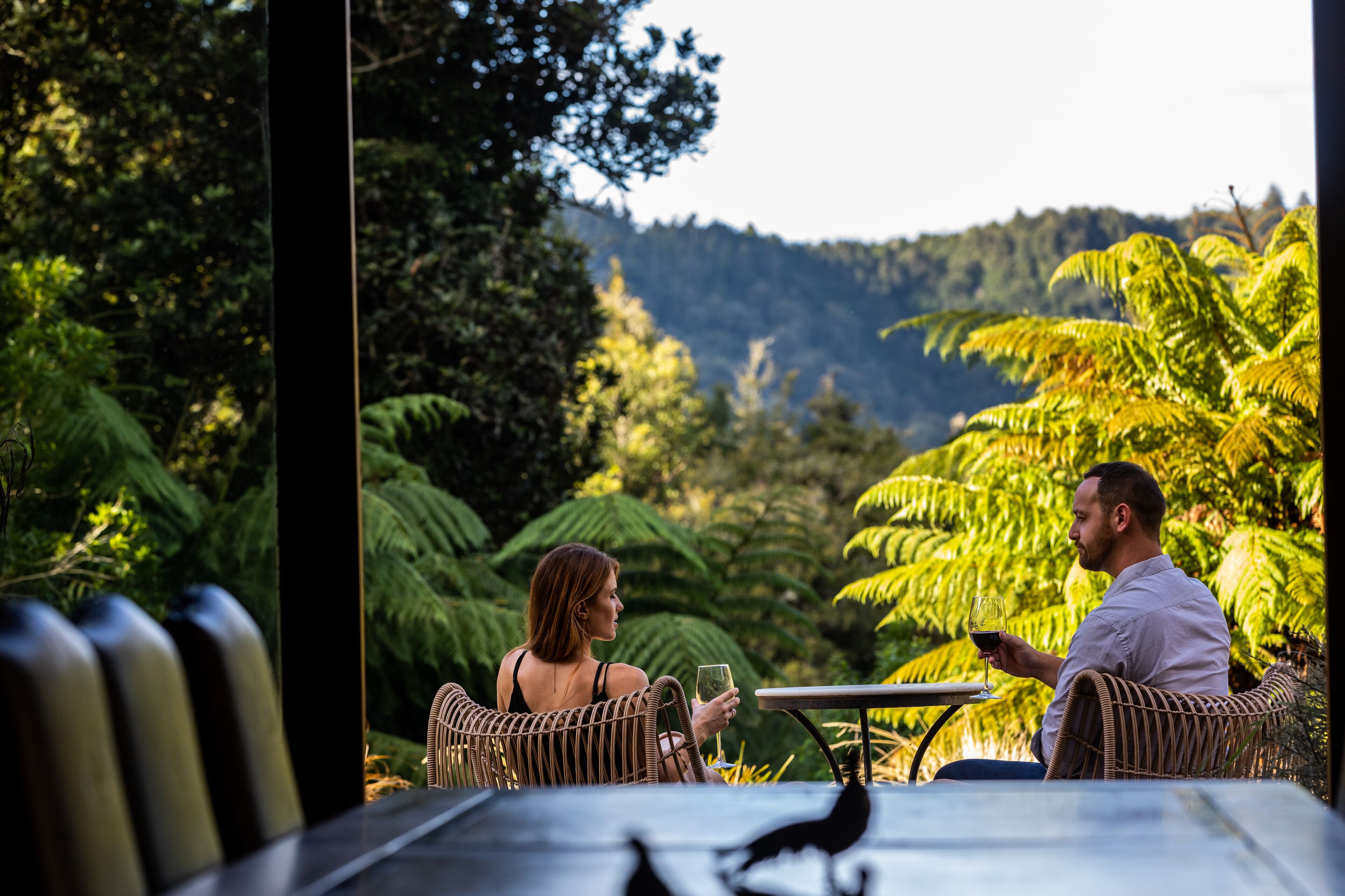 A couple seated at an outdoor table with a view of lush greenery and hills in the background.