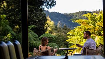 A couple seated at an outdoor table with a view of lush greenery and hills in the background.