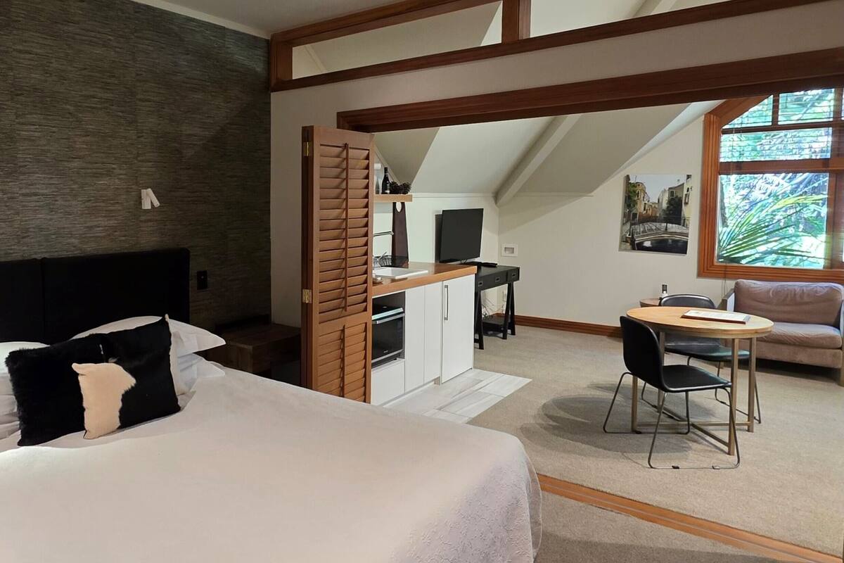 A bedroom with a bed, a desk, and a chair. There is a window with a view of greenery.