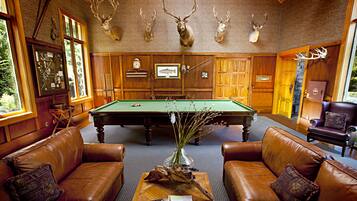 A billiards room with a pool table, leather sofas, and mounted deer heads on the wall.