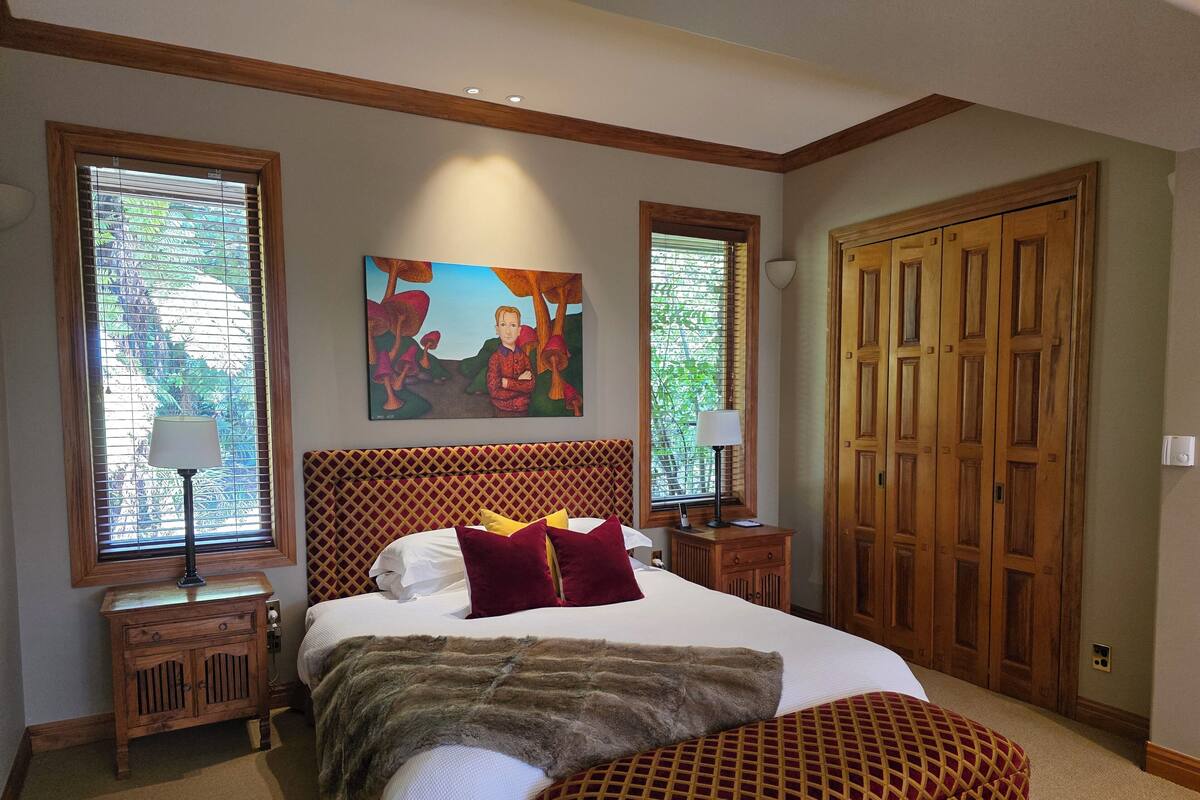 A bedroom with a large bed, two bedside tables, a wooden wardrobe, and a painting on the wall.