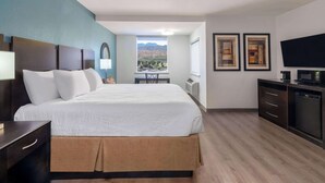 A hotel room with a large bed, a desk, a chair, a TV, and a window with a mountain view.