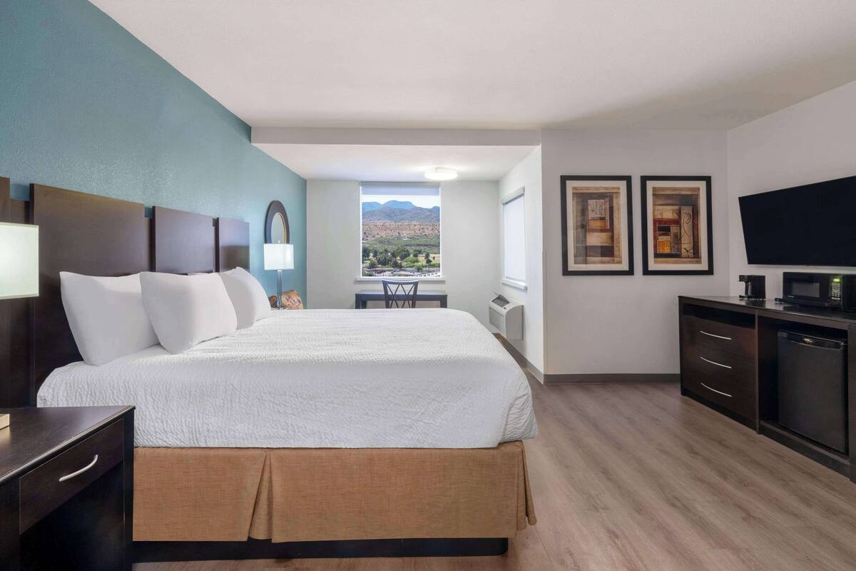 Ein Hotelzimmer mit einem großen Bett, einem Schreibtisch, einem Sessel, einem Fernseher und einem Fenster mit Blick auf die Berge.