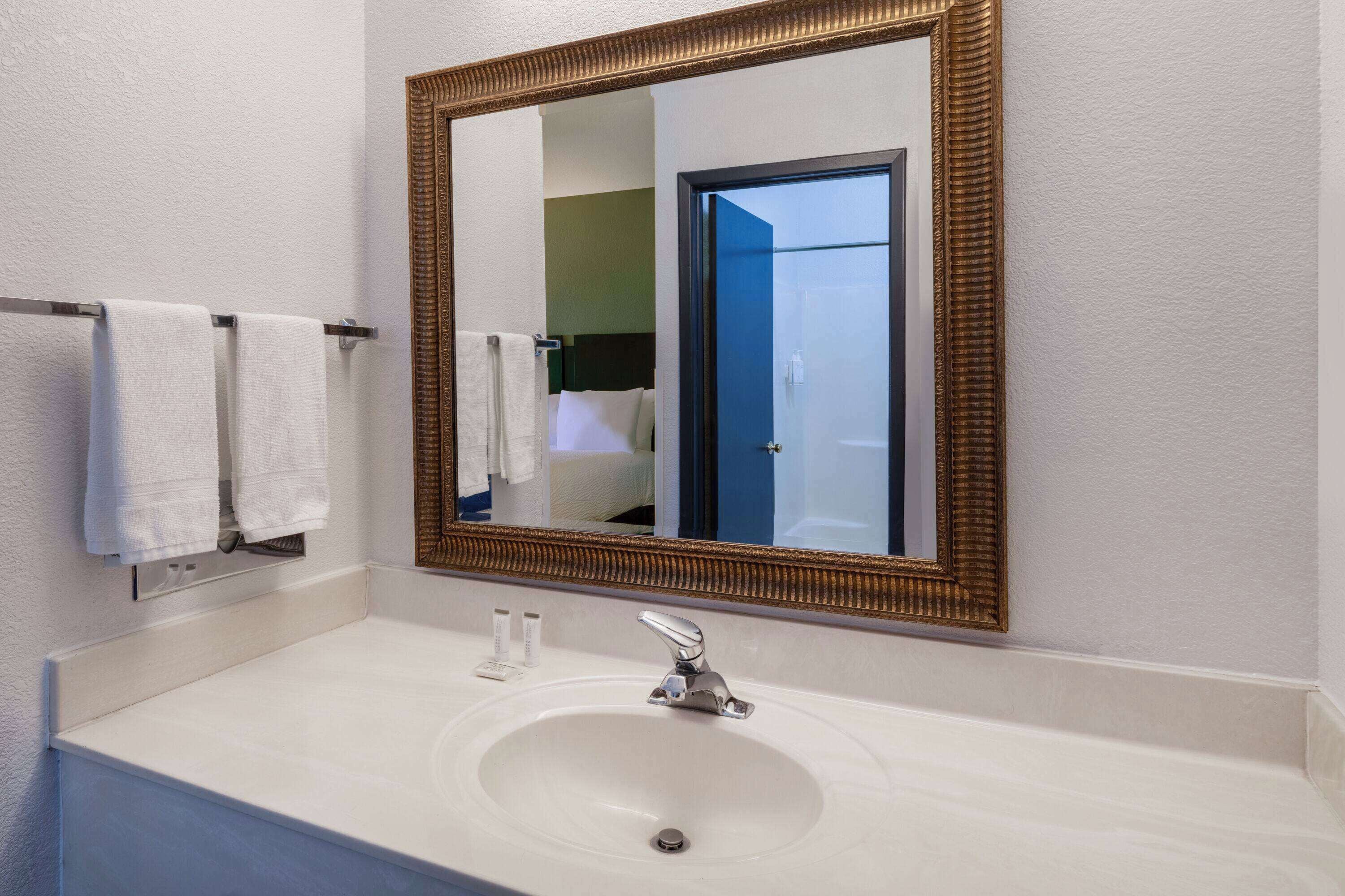 A bathroom with a white sink, a gold-framed mirror, and a towel rack with two white towels.