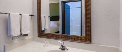 A bathroom with a white sink, a gold-framed mirror, and a towel rack with two white towels.