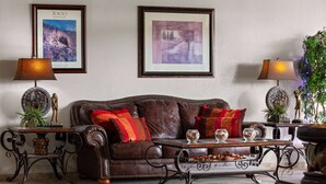 A living room with a brown leather sofa, two side tables with lamps, framed pictures on the wall, and a decorative plant.