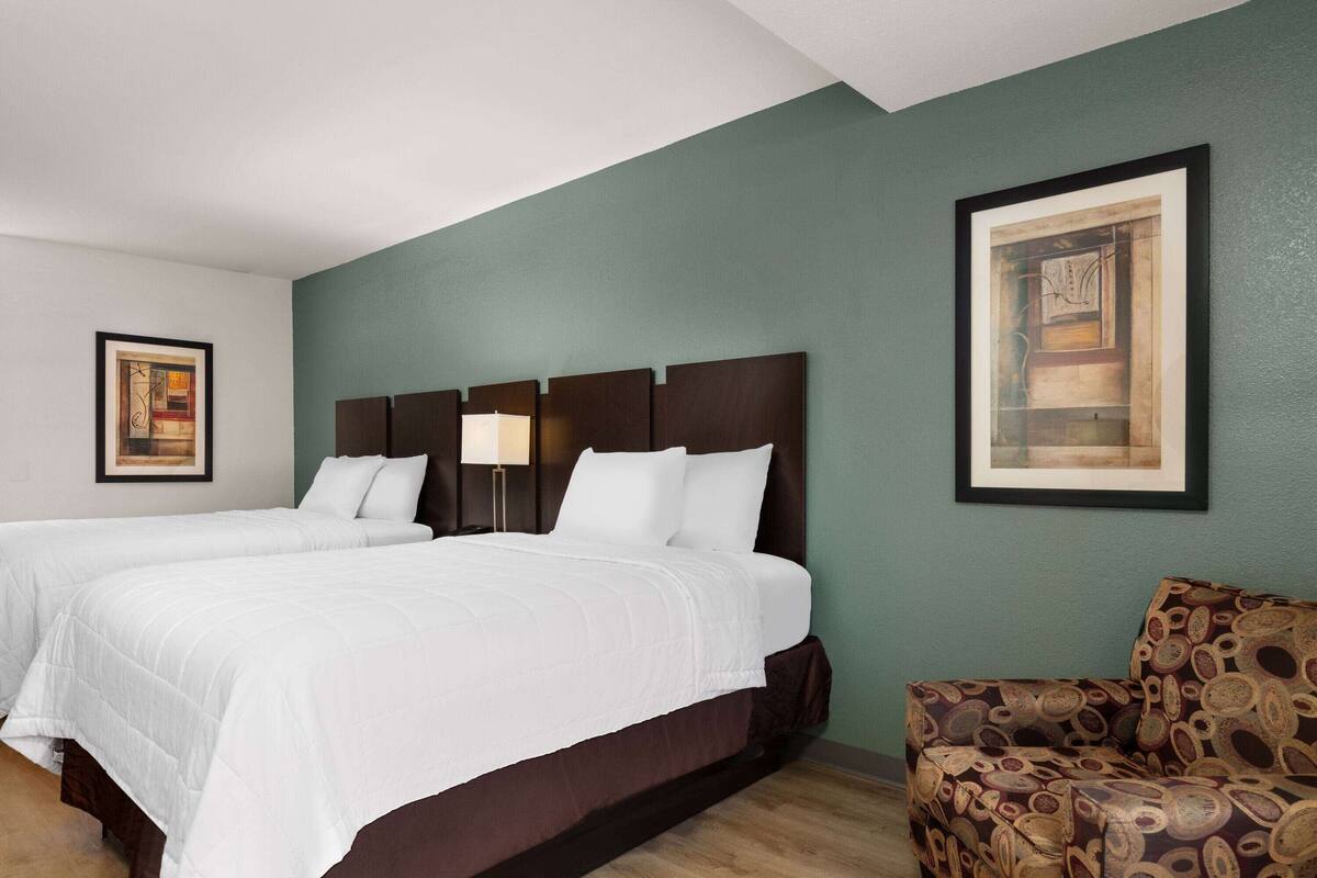 Ein Hotelzimmer mit zwei Betten, einem gemusterten Sessel und Bildern an den Wänden.