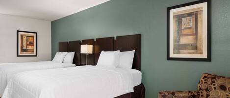 A hotel room with two beds, a patterned armchair, and artwork on the walls.